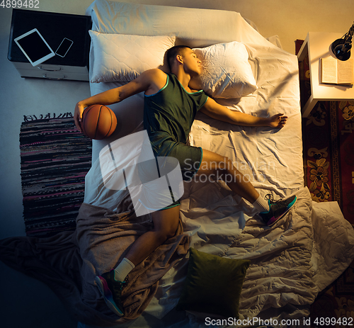 Image of Top view of young professional basketball player sleeping at his bedroom in sportwear with ball