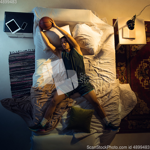 Image of Top view of young professional basketball player sleeping at his bedroom in sportwear with ball