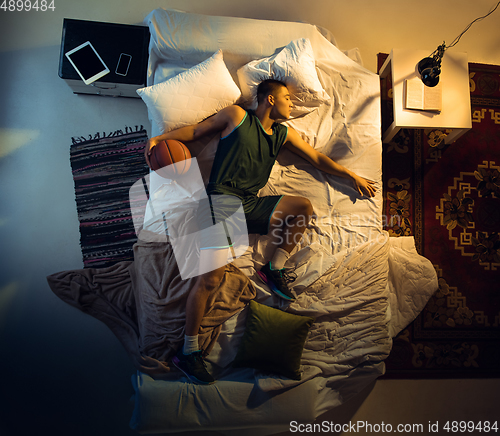 Image of Top view of young professional basketball player sleeping at his bedroom in sportwear with ball