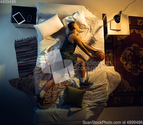 Image of Top view of young professional basketball player sleeping at his bedroom in sportwear with ball