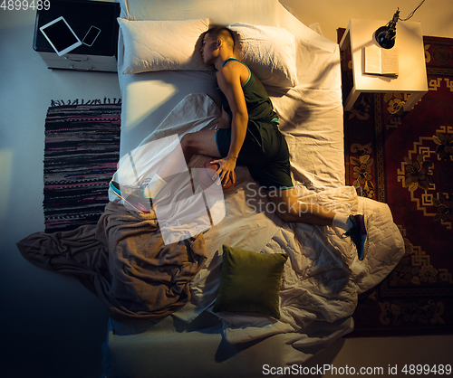 Image of Top view of young professional basketball player sleeping at his bedroom in sportwear with ball