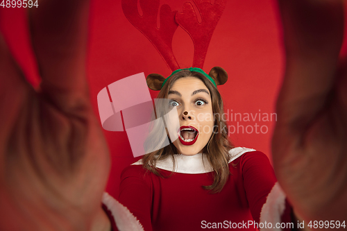 Image of Beautiful woman like Christmas deer isolated on red background. Concept of 2021 New Year\'s, winter mood, holidays.