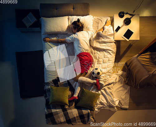 Image of Top view of young professional football, soccer player sleeping at his bedroom in sportwear with ball