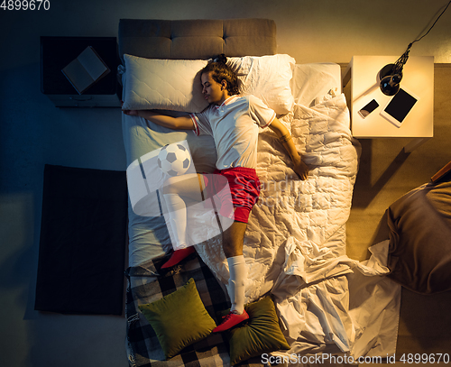 Image of Top view of young professional football, soccer player sleeping at his bedroom in sportwear with ball