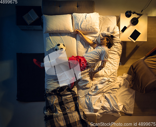 Image of Top view of young professional football, soccer player sleeping at his bedroom in sportwear with ball