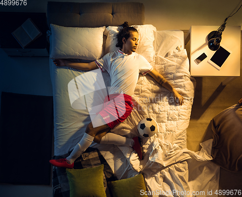 Image of Top view of young professional football, soccer player sleeping at his bedroom in sportwear with ball