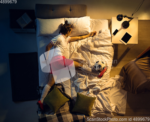 Image of Top view of young professional football, soccer player sleeping at his bedroom in sportwear with ball