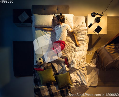 Image of Top view of young professional football, soccer player sleeping at his bedroom in sportwear with ball