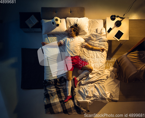 Image of Top view of young professional football, soccer player sleeping at his bedroom in sportwear with ball