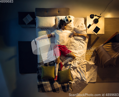 Image of Top view of young professional football, soccer player sleeping at his bedroom in sportwear with ball