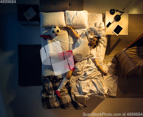 Image of Top view of young professional football, soccer player sleeping at his bedroom in sportwear with ball