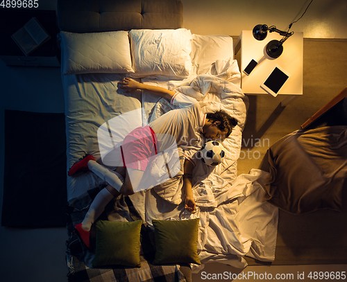 Image of Top view of young professional football, soccer player sleeping at his bedroom in sportwear with ball