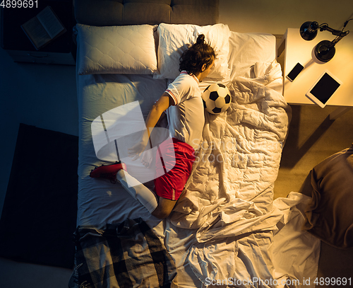 Image of Top view of young professional football, soccer player sleeping at his bedroom in sportwear with ball