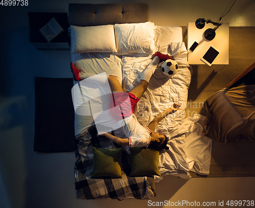 Image of Top view of young professional football, soccer player sleeping at his bedroom in sportwear with ball