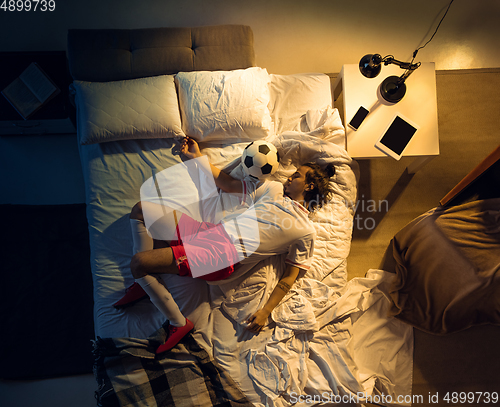 Image of Top view of young professional football, soccer player sleeping at his bedroom in sportwear with ball