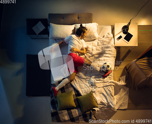 Image of Top view of young professional football, soccer player sleeping at his bedroom in sportwear with ball