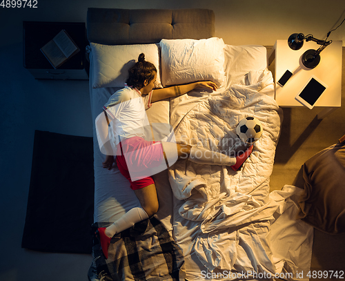 Image of Top view of young professional football, soccer player sleeping at his bedroom in sportwear with ball