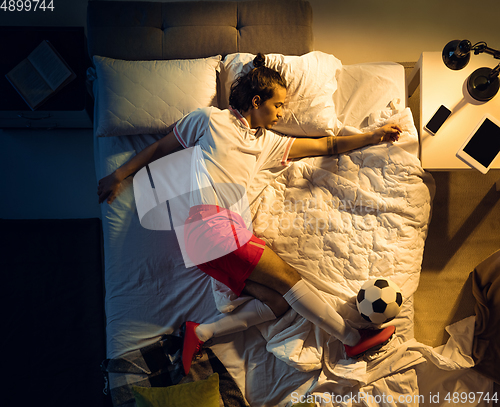 Image of Top view of young professional football, soccer player sleeping at his bedroom in sportwear with ball
