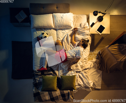 Image of Top view of young professional football, soccer player sleeping at his bedroom in sportwear with ball