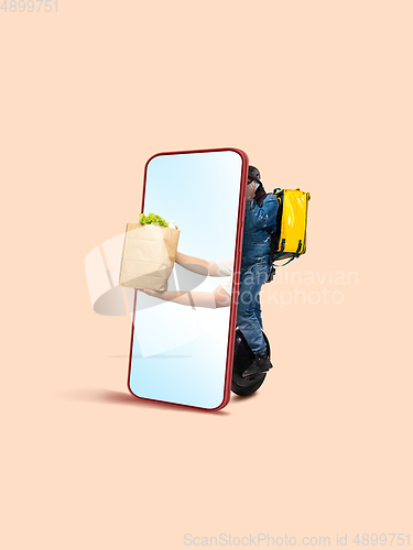 Image of Handsome delivery man giving order right from smartphone\'s screen, fast delivery concept