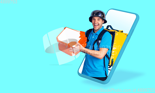 Image of Handsome delivery man giving order right from smartphone\'s screen, fast delivery concept