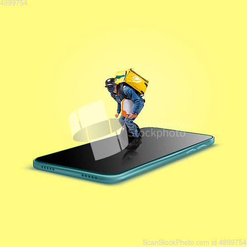 Image of Handsome delivery man giving order right from smartphone\'s screen, fast delivery concept