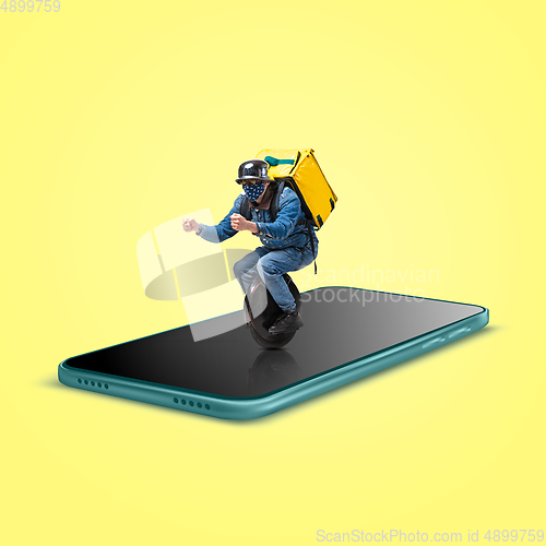 Image of Handsome delivery man giving order right from smartphone\'s screen, fast delivery concept