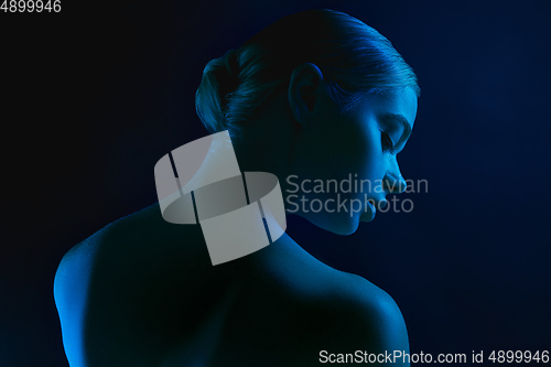 Image of Portrait of female fashion model in neon light on dark studio background.