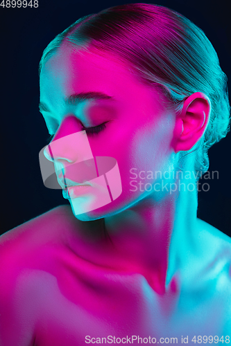 Image of Portrait of female fashion model in neon light on dark studio background.