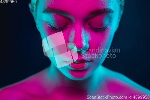Image of Portrait of female fashion model in neon light on dark studio background.