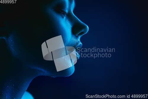 Image of Portrait of female fashion model in neon light on dark studio background.