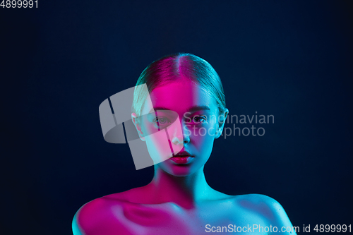 Image of Portrait of female fashion model in neon light on dark studio background.