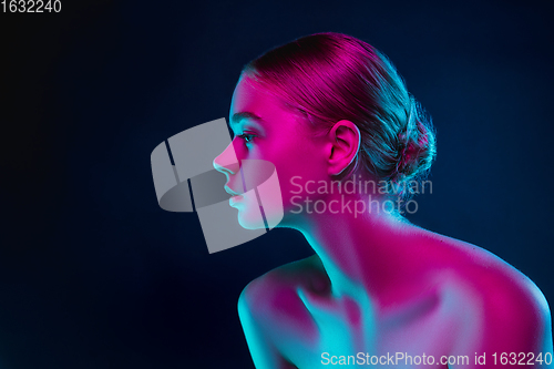 Image of Portrait of female fashion model in neon light on dark studio background.