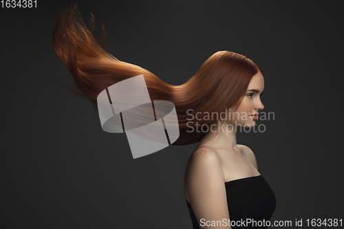 Image of Beautiful model with long smooth, flying red hair isolated on dark studio background.