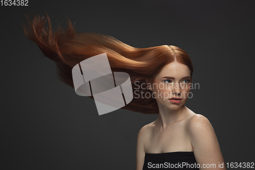 Image of Beautiful model with long smooth, flying red hair isolated on dark studio background.