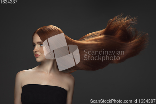 Image of Beautiful model with long smooth, flying red hair isolated on dark studio background.