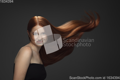 Image of Beautiful model with long smooth, flying red hair isolated on dark studio background.