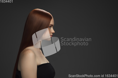 Image of Beautiful model with long smooth, flying red hair isolated on dark studio background.