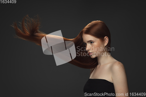 Image of Beautiful model with long smooth, flying red hair isolated on dark studio background.