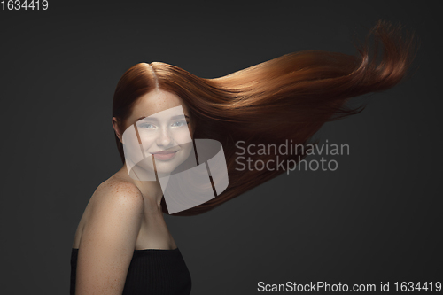 Image of Beautiful model with long smooth, flying red hair isolated on dark studio background.