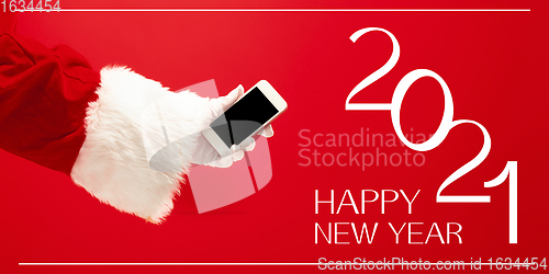 Image of Hand of Santa Claus holding phone, greeting with New Year 2021 and Christmas. Flyer with copyspace