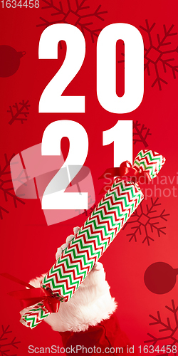 Image of Hand of Santa Claus holding gift, greeting with New Year 2021 and Christmas. Flyer with copyspace