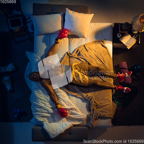 Image of Top view of young professional boxer, fighter sleeping at his bedroom in sportwear with gloves