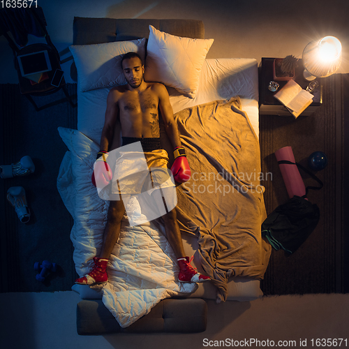 Image of Top view of young professional boxer, fighter sleeping at his bedroom in sportwear with gloves