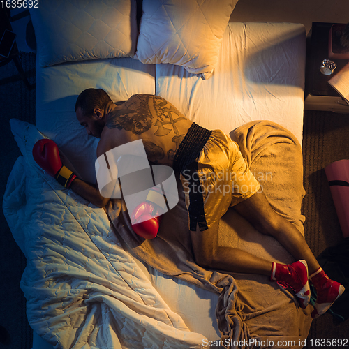 Image of Top view of young professional boxer, fighter sleeping at his bedroom in sportwear with gloves