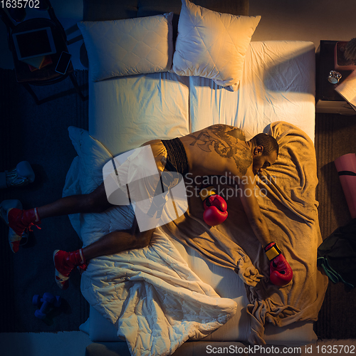 Image of Top view of young professional boxer, fighter sleeping at his bedroom in sportwear with gloves