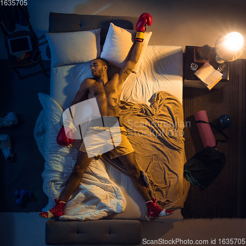 Image of Top view of young professional boxer, fighter sleeping at his bedroom in sportwear with gloves