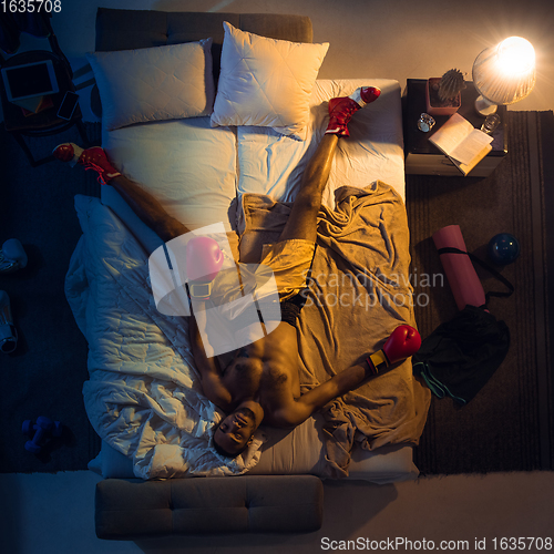 Image of Top view of young professional boxer, fighter sleeping at his bedroom in sportwear with gloves