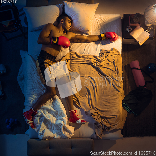 Image of Top view of young professional boxer, fighter sleeping at his bedroom in sportwear with gloves