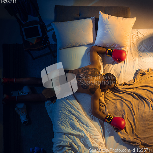 Image of Top view of young professional boxer, fighter sleeping at his bedroom in sportwear with gloves